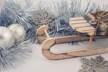 Christmas or New Year decorations (silver tinsel, snowflakes and a wooden toy Christmas sleigh on a white wooden background), retro toned, vintage style