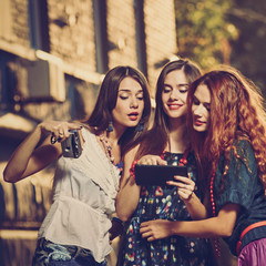 Three happy attractive women looking photos on tablet, image with warm vintage toning and square...