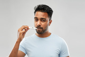 people, healthcare and fever concept - unhealthy indian man measuring oral temperature by thermometer over grey background - obrazy, fototapety, plakaty