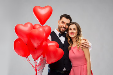Fototapeta na wymiar valentines day, love and people concept - happy couple with red heart shaped balloons over grey background
