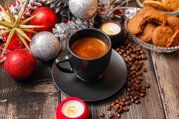 Black cup of coffee, cookies filled with chocolate, Christmas balls, candles and coffee beans. Close-up on the old rustic wooden table
