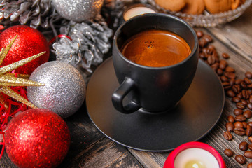 Black cup of coffee, cookies filled with chocolate, Christmas balls, candles and coffee beans. Close-up on the old rustic wooden table