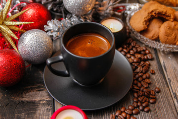 Black cup of coffee, cookies filled with chocolate, Christmas balls, candles and coffee beans. Close-up on the old rustic wooden table