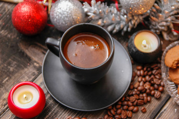 Black cup of coffee, cookies filled with chocolate, Christmas balls, candles and coffee beans. Close-up on the old rustic wooden table