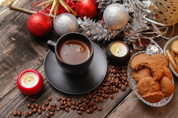 Obraz na płótnie Canvas Black cup of coffee, cookies filled with chocolate, Christmas balls, candles and coffee beans. Close-up on the old rustic wooden table