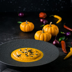 Pumpkin orange cream soup in black plate. Dark photo