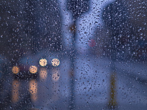 Rain drops on bus stop window and far side visible car lights. Cold rainy day waiting bus stop after work