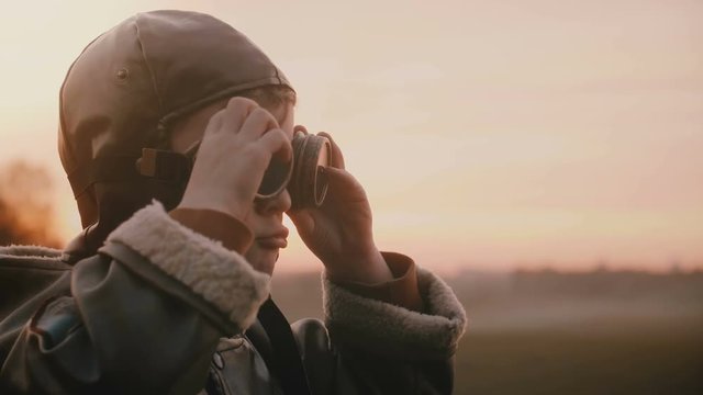 Little happy boy in fun old pilot costume wearing retro aviation glasses making silly faces in sunset field slow motion.