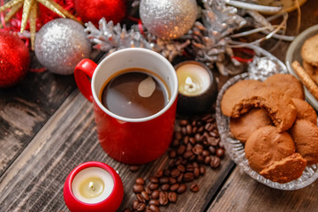 Big red cup of coffee, cookies filled with chocolate, Christmas balls, candles and coffee beans. Close-up on the old rustic wooden table