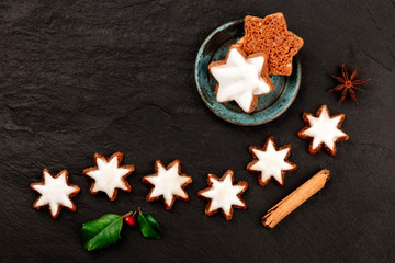 Zimsterne, traditional German cinnamon star cookies, shot from the top on a black background with anise, cinnamon, holy leaves and a place for text