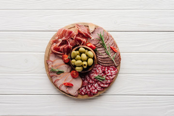 top view of arrangement of various meat snacks and olives on white wooden backdrop
