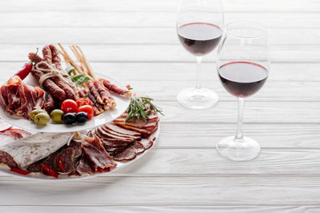 close up view of glasses of red wine and delicious meat snacks on white wooden tabletop
