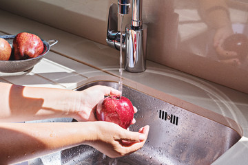 Female hands washing red apple in water stream in kitchen metallic sink