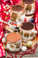 Tiramisu in glass cups, surrounded by red, gold and silver Christmas decorations