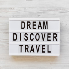 Modern board with text 'Dream Discover Travel' word over white wooden surface, top view. From above, flat lay, overhead.