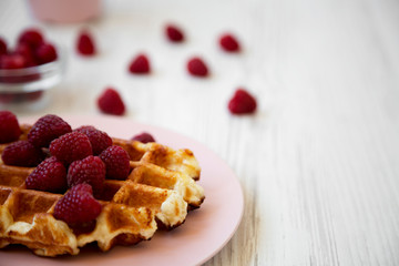 Traditional belgian waffle with raspberries on pink plate over white wooden background, side view. Close-up. Copy space.