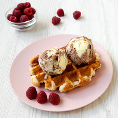 Traditional belgian waffle with icecream and raspberries on pink plate, side view. Closeup.