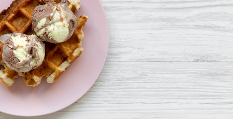 Traditional belgian waffle with icecream on pink plate over white wooden surface, top view. Copy space.