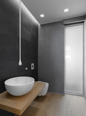 in the foreground the countertop sink that leaning against on the wooden top and the modern faucet pending from the ceiling in the bathroom with wooden floor