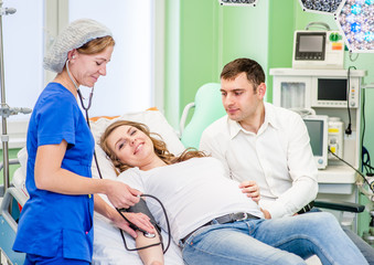 Fototapeta premium Nurse measuring pressure of pregnant woman. Husband supports pregnant wife for examination