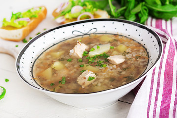 Buckwheat soup with chicken  in a plate, bread with mustard ang red onion on a wooden white table.