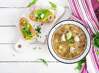 Buckwheat soup with chicken  in a plate, bread with mustard ang red onion on a wooden white table....