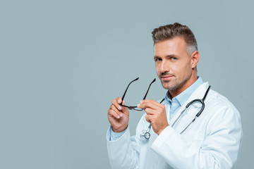 handsome doctor with stethoscope holding glasses and looking at camera isolated on white