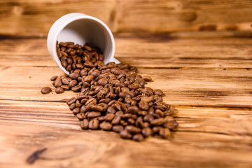 White cup and scattered coffee beans on wooden table