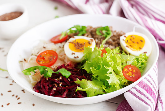 Buckwheat porridge buddha bowls with beetroot, cabbage, boiled eggs and  fresh tomato on white table. Healthy breakfast.