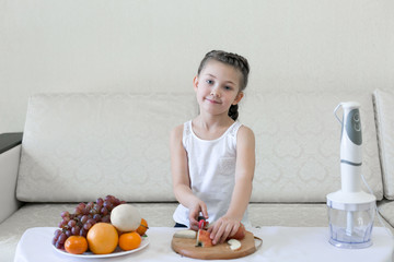 The child cuts apples with a knife. The girl cuts with a knife the fruit for making juice.