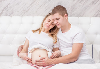 Happy pregnant woman and her husband with headphones on tummy playing music to her baby