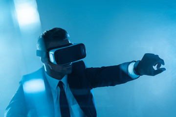 businessman in virtual reality headset touching something isolated on blue, artificial intelligence concept