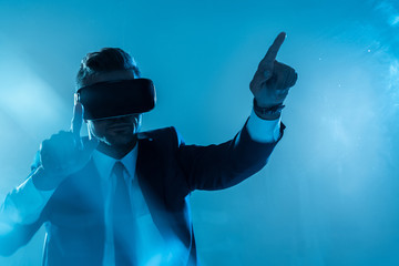 businessman in suit and virtual reality headset touching something isolated on blue, artificial intelligence concept