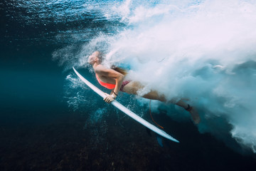 Attractive surfer woman dive underwater with under barrel wave and bubbles.
