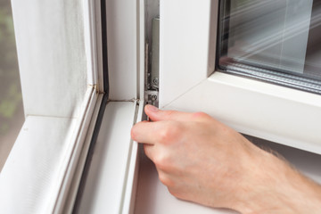 Handyman repairs plastic window with a hexagon. Workman adjusts the operation of the plastic window.