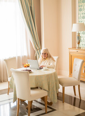 Senior woman at the laptop relaxing at home sitting at the table