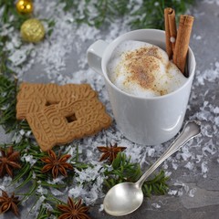 Tasse Kakao mit aufgeschäumter Milch, Zimtstangen, Spekulatius-Plaätzchen und Sternanis auf einem...