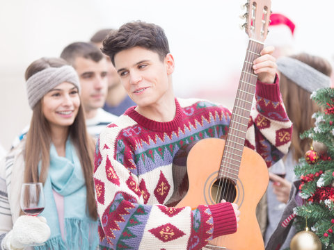 Young man with friends on Christmas,playing guitar - Powered by Adobe