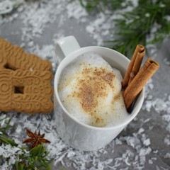 Obraz na płótnie Canvas Tasse Kakao mit aufgeschäumter Milch, Zimtstangen, Spekulatius-Plaätzchen und Sternanis auf einem verschneiten Gartentisch