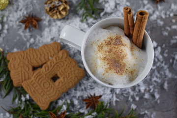 Tasse Kakao mit aufgeschäumter Milch, Zimtstangen, Spekulatius-Plaätzchen und Sternanis auf einem verschneiten Gartentisch