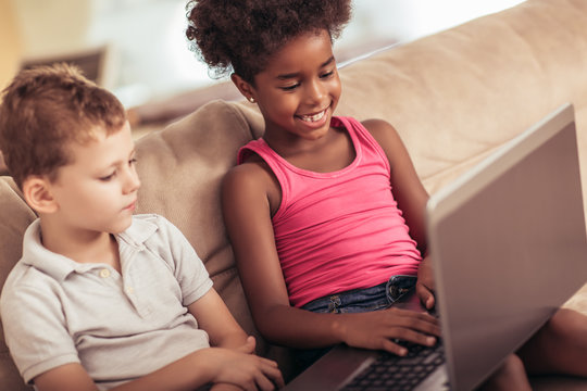 Caucasian boy and African American girl at home using laptop.