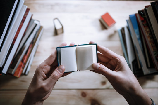 A man reading a miniature book among the big books in the library