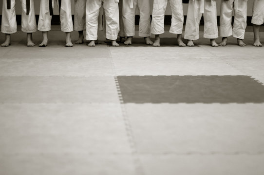 a slender row of young karatekas before the exam. Children in Kimano on tatami. Black and white photo without faces with space for text.
