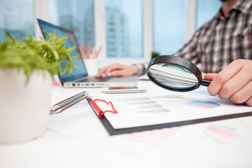 Businessman analyzing business graphs with magnifying glass