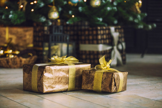 Christmas Gifts In Golden Wrapping Paper Lie Under The Christmas Tree Decorated On The Floor