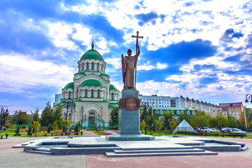 Beautiful colorful square in front of the Christian church in the city center on a cloudy day with thick blue clouds. Monument to Saint Vladimir the Baptist and Vladimir Cathedral, Astrakhan, Russia. - obrazy, fototapety, plakaty