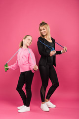 sporty mother and adorable daughter holding jump ropes, isolated on pink