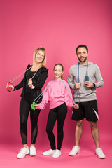 parents and daughter in sportswear holding skipping ropes, isolated on pink