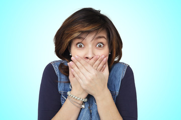 Asian girl closes hands over her mouth in shock by what she heard standing on bright blue background. Keep secret carefully