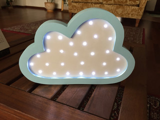 A beautiful soft blue nightlight in the shape of a cloud is standing on a textural wooden table